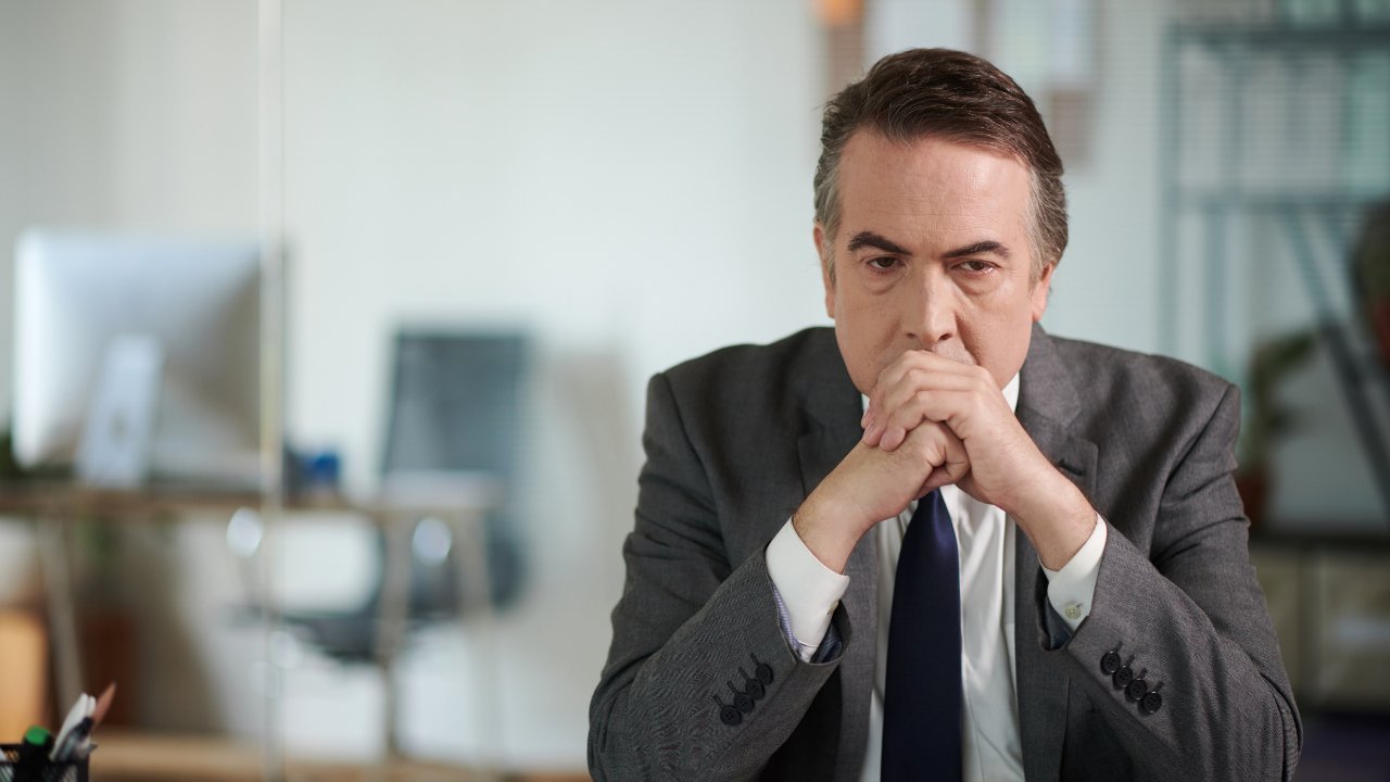 A senior executive pausing at his desk, weighed down by competing priorities